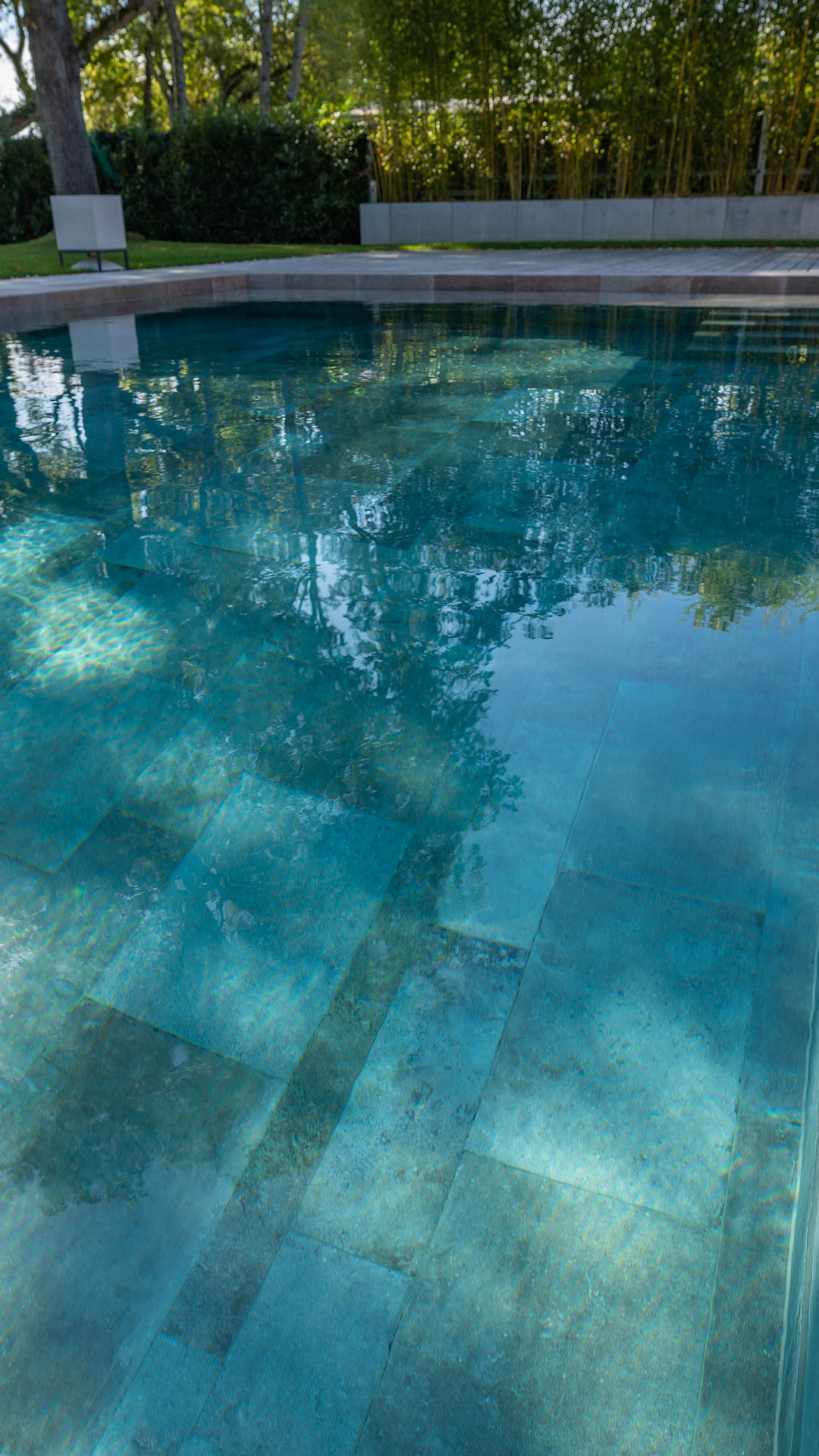 Couleur eau piscine verte avec carrelage taupe et ombres des arbres à Lausanne